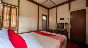Un dormitorio con una cama con almohadas rojas y un televisor. en OYO 93277 Villa Kemiloko Syariah, en Prigen