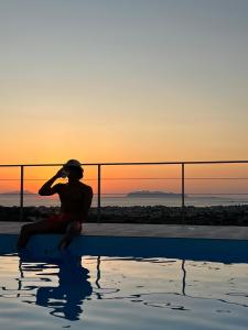 a man sitting next to a pool with the sunset at Villa Demirà - Boutique Rooms & Panoramic Pool in Marsala