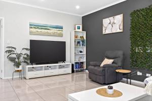 a living room with a flat screen tv and a chair at Reef Retreat - Modern Beach House Sanctuary in Port Noarlunga