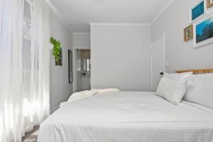 a white bedroom with a white bed and a window at Reef Retreat - Modern Beach House Sanctuary in Port Noarlunga