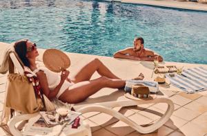 Un hombre y una mujer sentados junto a una piscina en Beneste Villa Flamenca Hotel, en Nerja