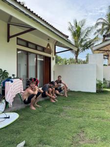a group of people sitting on the grass outside of a house at Walur Surf Villa II in Wainapal