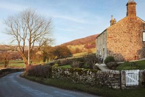 a brick house with a stone wall next to a road at Wharfe View Cottage Bolton Abbey Estate in Skipton