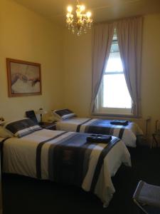 2 Betten in einem Zimmer mit einem Fenster und einem Kronleuchter in der Unterkunft Lancefield Guest House in Lance Field