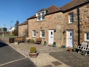 een oud bakstenen huis met witte deuren en banken bij Kingsbarns Apartment in Kingsbarns