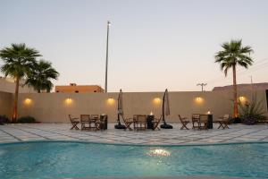 a pool with tables and chairs and palm trees at Jovan Suites apartment 2 in AlUla