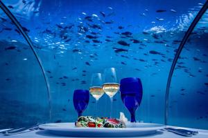 a table with a plate of food and two glasses of wine at Hurawalhi Island Resort in Kuredu