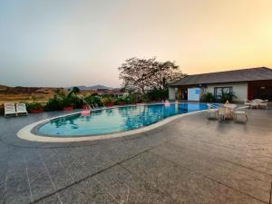 a large swimming pool with chairs and a house at Touchwood Bliss Nature Retreat - Igatpuri in Igatpuri