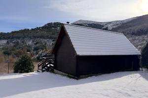 a black barn in the snow with mountains in the background at Cabaña Las Víboras Sierra Nevada in Güéjar-Sierra