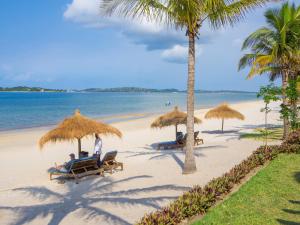 a group of people sitting on a beach with umbrellas at San Martinho Vila Azul in Vila Praia Do Bilene