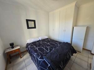 a bedroom with a bed and a table and a refrigerator at Hermanus Beach Club in Hermanus