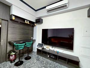 Una sala de estar con un televisor grande y dos taburetes verdes. en 東港包棟 悠舍民宿, en Donggang