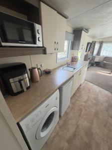 a kitchen with a washing machine and a microwave at Sunnymede D1 - Hot Tub Caravan - Sleeps 10 - Fantasy Island, Ingoldmells - Meadow Lakes Caravan & Lodge Hire in Ingoldmells