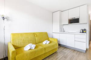a yellow couch in a living room with a kitchen at Hostdomus - Yellow Suite in Sestriere