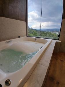 a bath tub in a bathroom with a large window at Scandinavian Lodge - Jacuzzi Privativa in Campos do Jordão
