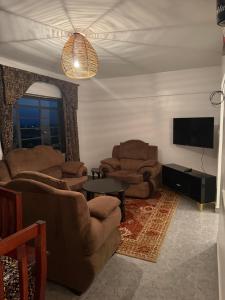 Nzuri Apartment في كيزيمو: غرفة معيشة مع كنب وتلفزيون وطاولة