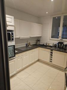 Chambre d'hôte dans appartement Lyon 69006 في ليون: مطبخ مع خزائن بيضاء وقمم منضدة سوداء