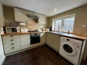 una cucina con mobili bianchi, lavatrice e asciugatrice di Daisy Cottage - Framlingham a Framlingham