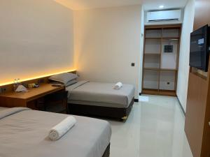 a room with two beds and a desk and a television at Passifika Hotel Maluk in Maluk