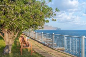 a woman sitting in a chair under a tree next to the ocean at Baía II by An Island Apart in Funchal +36 photos
