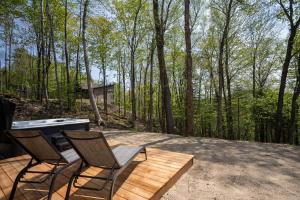 two chairs and a grill on a wooden deck in the woods at Chalet du Golf avec Spa in Saint-Faustin