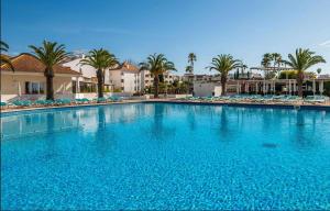 a large blue swimming pool with palm trees and buildings at Golden Refúgio das Andorinhas in Cabanas de Tavira