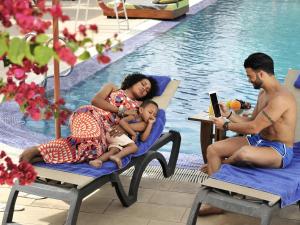 a family sitting on chairs next to a swimming pool at Pullman Dakar Teranga in Dakar