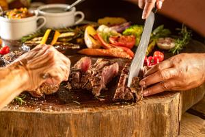 a person cutting a steak on a table with a knife at Pousada Fazenda Aroeira Secretário in Itaipava