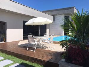 um deque de madeira com uma mesa, cadeiras e um guarda-sol em Linda casa com piscina - locação temporada em itapoá sc em Itapoa
