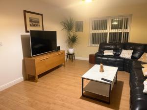 a living room with a black leather couch and a flat screen tv at Swn yr Coed in Sennybridge