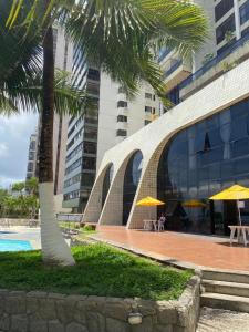 un palmier devant un bâtiment avec des tables et des parasols dans l'établissement Suíte Golden Beach Frente Mar, à Récife