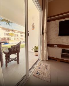Una puerta corrediza de vidrio que da a una sala de estar con un televisor. en SW Rustica Apartamentos, en Canoa Quebrada