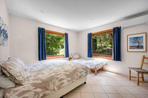 a bedroom with a bed and a chair and two windows at Sweeds - Belle Escapes Jervis Bay in Vincentia