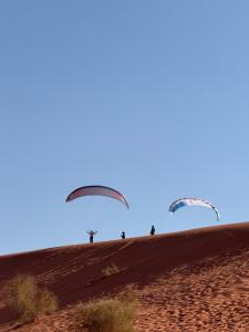 two paragliders are flying over a dirt hill at Natalie Wadi Rum camp & Jeep tour in Wadi Rum