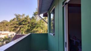 a green house with a balcony with a window at Quarto do Sol Relaxante - 150m da praia in Ubatuba