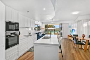 a kitchen with white cabinets and a table and a dining room at Poolside Bliss in Maroochydore