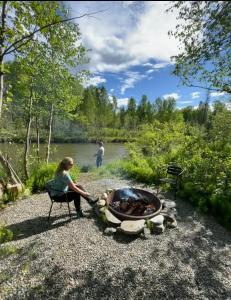 a woman sitting in a chair next to a fire pit at Riverfront, Authentic, Luxury Log Cabin-Black Bear in Wasilla