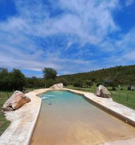 una piscina de agua con rocas en un campo en Cabañas Agua de Piedra, en Villa Giardino