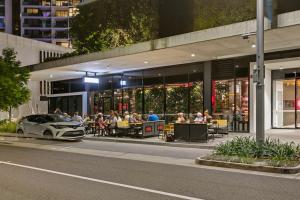 a car parked in front of a building with people sitting at tables at The Corso - Central Maroochydore Apartment in Maroochydore