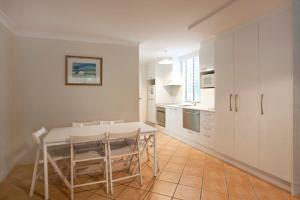 Blueys Beach Villa Manyana 24 في بلويز بيتش: مطبخ مع خزائن بيضاء وطاولة وكراسي