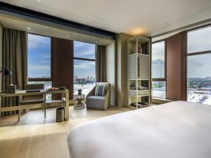 a bedroom with a bed and a desk and windows at Novotel Shanghai Clover in Shanghai