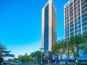 a tall building with trees in front of it at Xana Hotelle Xi'an 2nd Fengcheng Road Municipal Library Metro Station in Xi'an