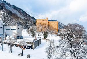 a building in the snow in front of a mountain at AURA YUZAWA Apartment Hotel - Spacious 1Bedroom Apartment with Large Living Room Sleeps 4 to 6, Bedroom with 2-Double Beds, Living Room with 1-Double Bed & 1-Sofa Bed in Yuzawa