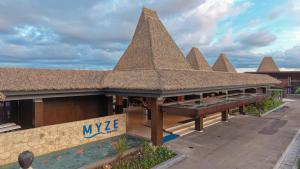 a building with a straw roof with a pool at Myze Hotel Waingapu in Waingapu