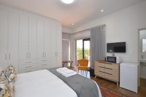 a white bedroom with a bed and a tv at Caracal 54 in Yzerfontein