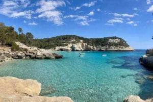 a beach with a boat in the water at Forcat - Apartamento con jardín y piscina in Ciutadella