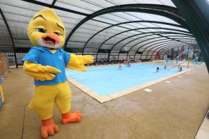 a mascot standing in front of a swimming pool at Camping Le Val de Trie in Béhen