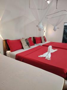 Peacock's Paradise Safari Hostel في اوداوالاوي: غرفة بسريرين ذات أغطية حمراء وبيضاء
