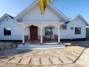 a white house with a porch and a palm tree at Malaika White House Apartment & Spa in Kiwengwa