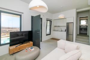a living room with a white couch and a tv at Rockaine Suites Sunset in Agios Fokas